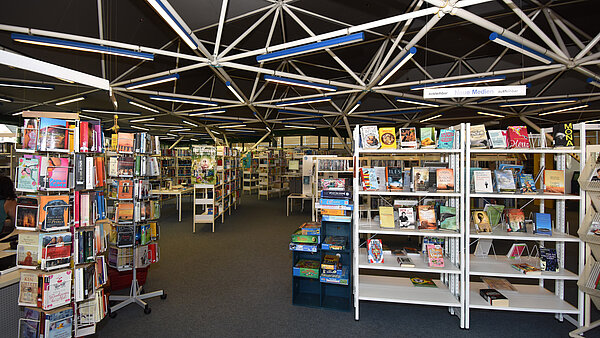 Innenansicht der Stadtteilbibliothek Neureut. Volle Bücherregale und Drehständer mit Taschenbüchern sind zu sehen.