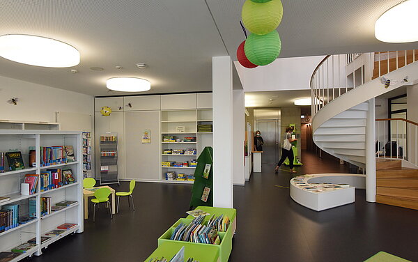 Hier ist der untere Bereich von Seiten der Fensterfront abgebildet. Rechts sieht man die Wendeltreppe, links Bücherregale und mittig deutet sich die grüne Sitzbank des Kinderbereichs an