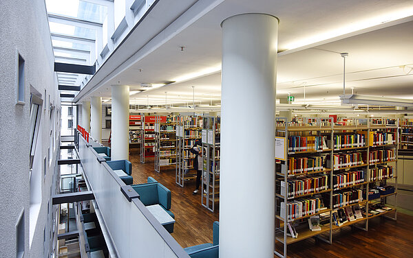 Blick auf das zweite Obergeschoss im Neuen Ständehaus. Man sieht volle Bücherregale, blaue Lesesessel und die Oberlichter durch die viel Tageslicht fällt.