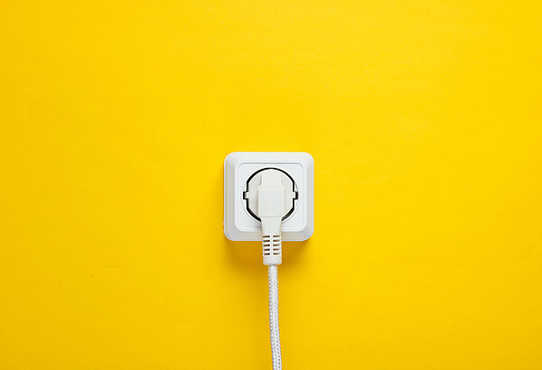 Weißes Kabel in weiße Steckdose gesteckt an gelber Wand